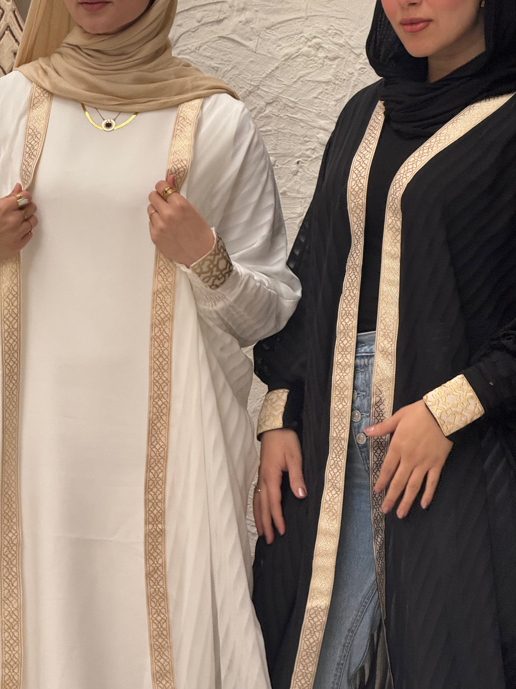 Two people wearing traditional outfits with intricate designs on a neutral background